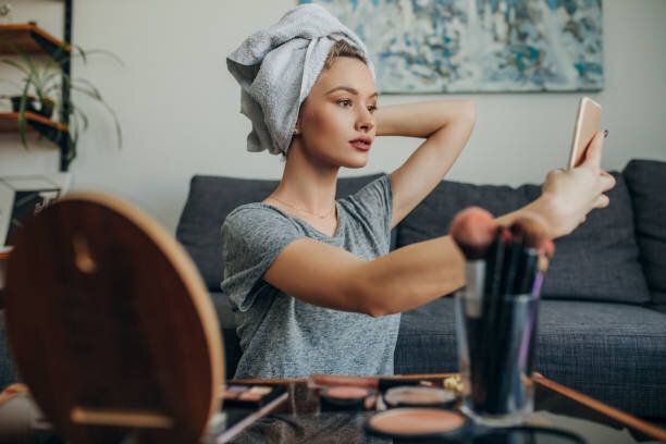 メイクアップ自分撮りを作成する彼女のアパートの若い女性