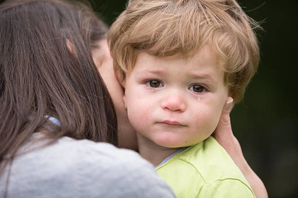 悲しい小さな男の子彼の母親に囲まれています。