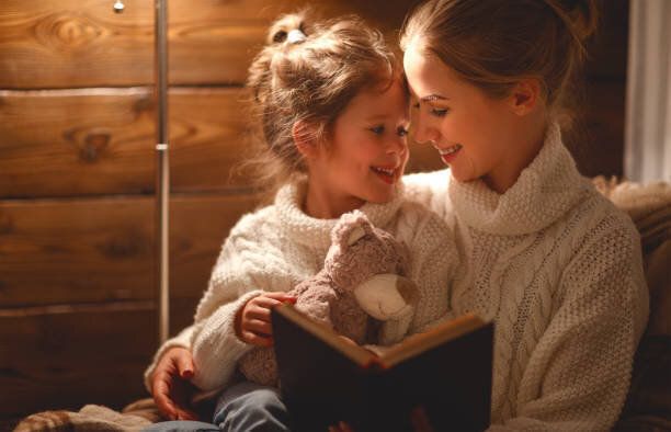 幸せな家族の母と子の娘が冬の夜に本を読む