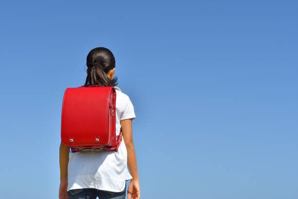 青空に立つ日本の小学生の女の子(後方の眺め)