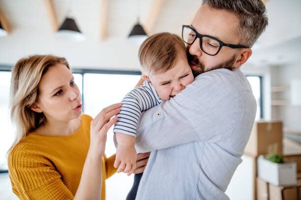 家庭で屋内に立って泣いている幼児の女の子と若い家族。
