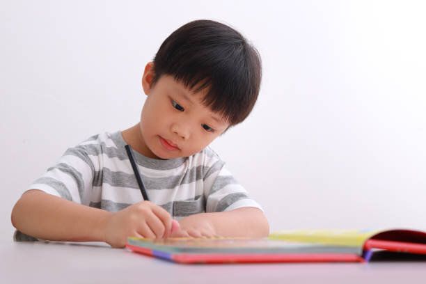 机の上の小さな男の子が白い背景に対して宿題をしている。