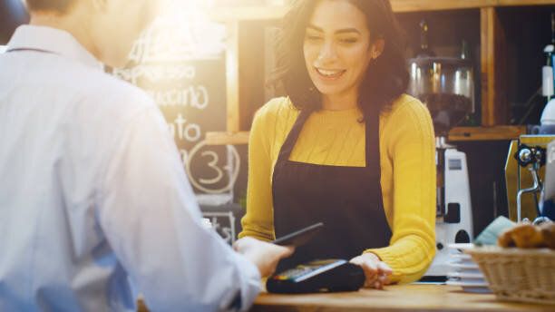カフェで美しいヒスパニック系女性は、コーヒーのテイクアウトを非接触の携帯電話で支払う客のクレジット カード システム。
