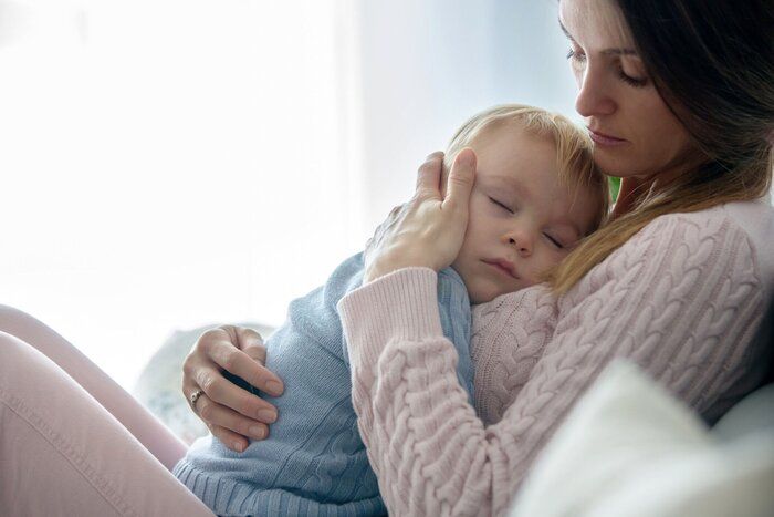 若い母親は、彼女の病気の幼児の男の子を抱きしめ、自宅で彼を抱きしめる