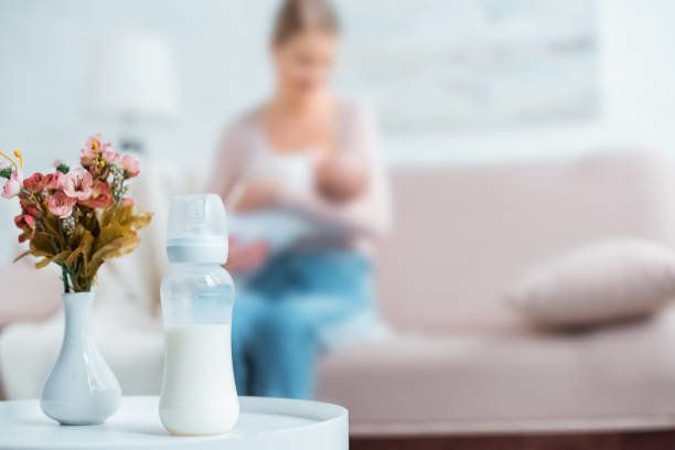 ミルクと哺乳瓶のクローズアップビュー、花瓶の花と自宅での母親の母乳育児の赤ちゃん