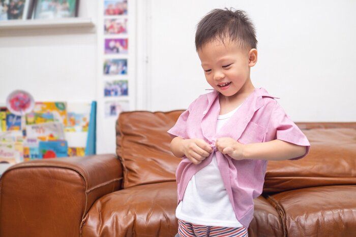 アジアの3-4歳の幼児の男の子は、自宅でシャツ(制服)を着用することに集中