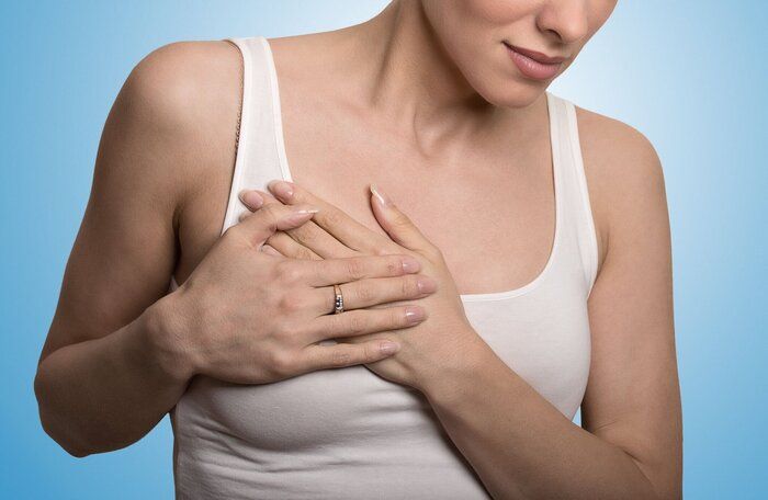 胸の痛みを持つクローズアップトリミングされた肖像画の若い女性は、青色の背景に孤立した胸に触れる