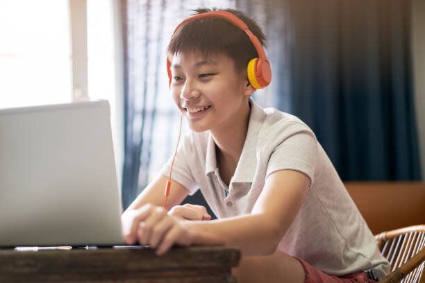 ヘッドセットを身に着けている自宅でオンラインレッスンを受けるアジアの10代の少年