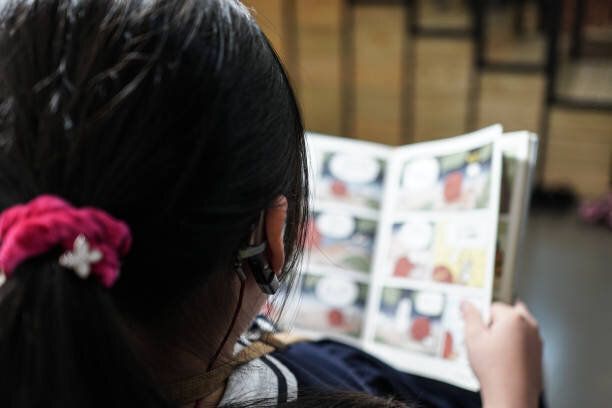 小さな女の子が図書館で読書をしています。補聴器で。