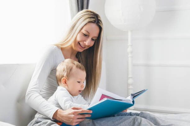 子供の教育。ベッドの上に座って、本を読んで、彼女の幼児を持つ母