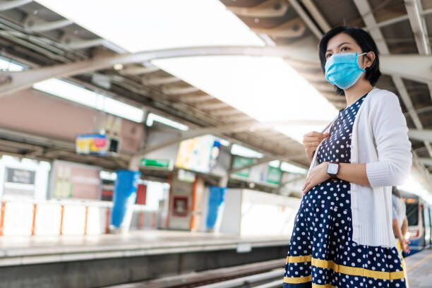 アジア妊娠女性は新しい正常で空の列車を待ってフェイスマスクを身に着けている