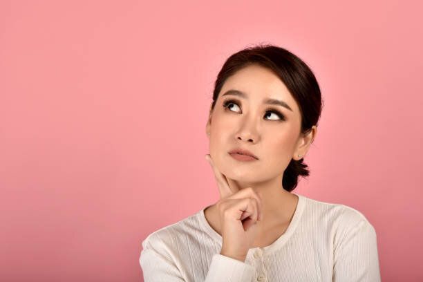 孤立したピンクの背景を考えるアジアの女性、女の子の顔の表情感の肖像画は疑問と不思議に感じています。