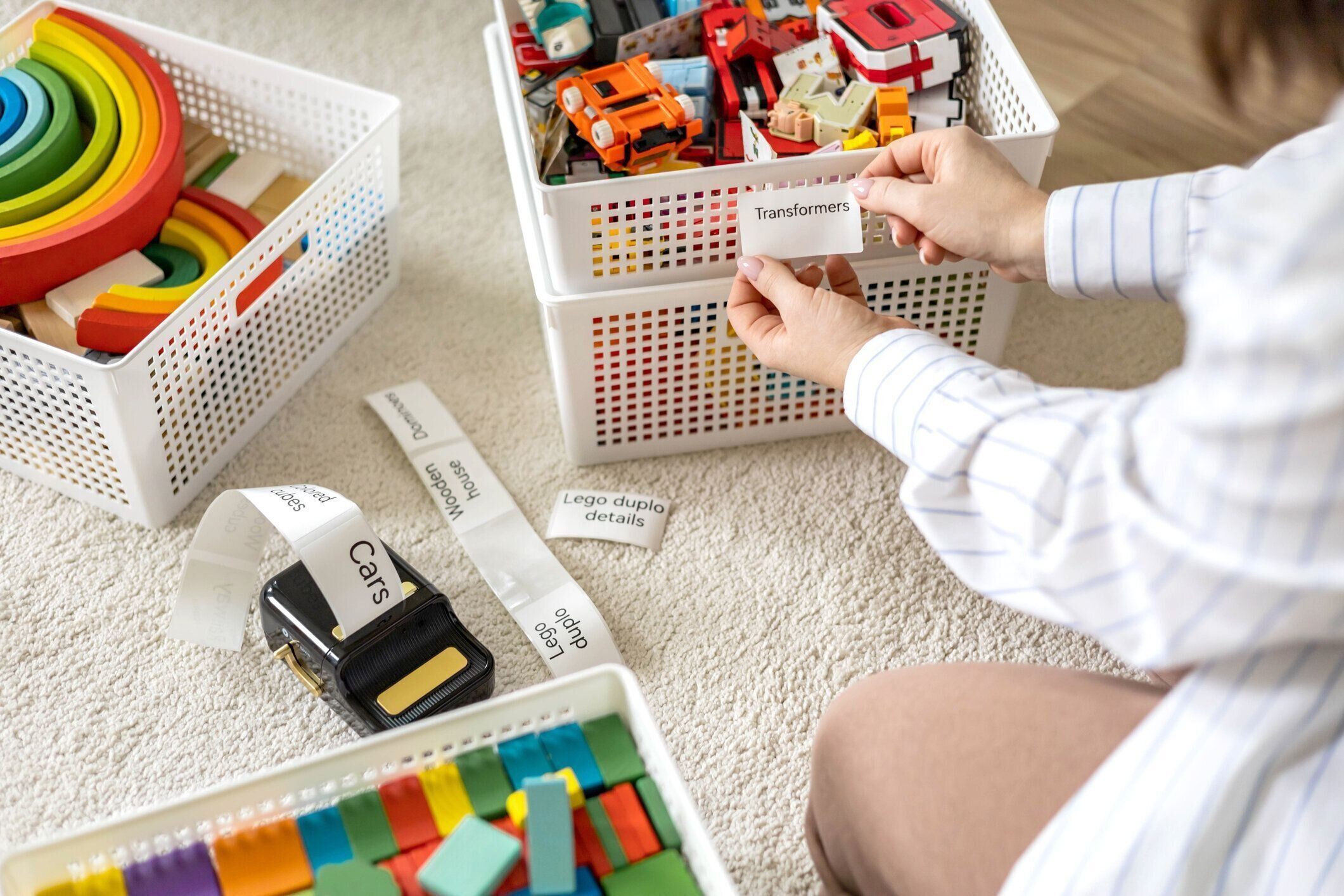 女性は子供っぽい部屋を掃除し、木製とプラスチックのおもちゃを分類し、モバイルラベルプリンターのステッカータイトルを使用します