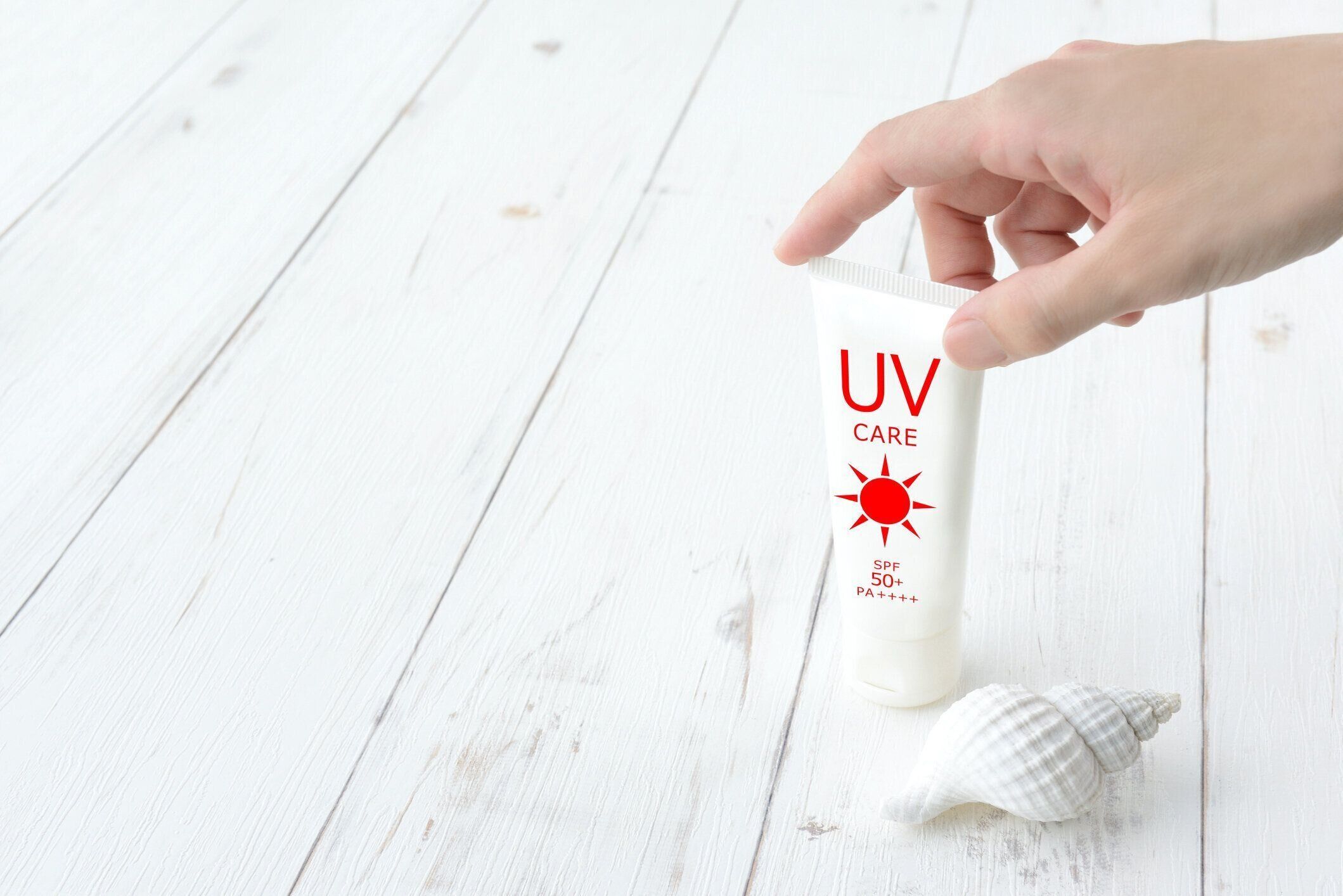 白い木製のボード上の日焼け止めクリームとシェルを選ぶ女性の手