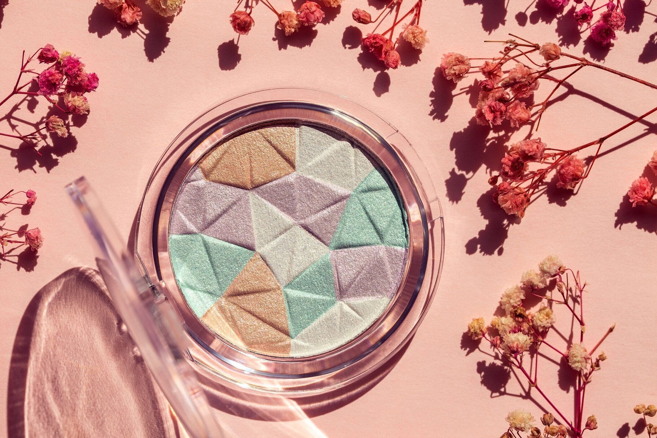 きらめきのあるライトアイシャドウ。乾燥した繊細な花を持つピンクの背景に化粧品