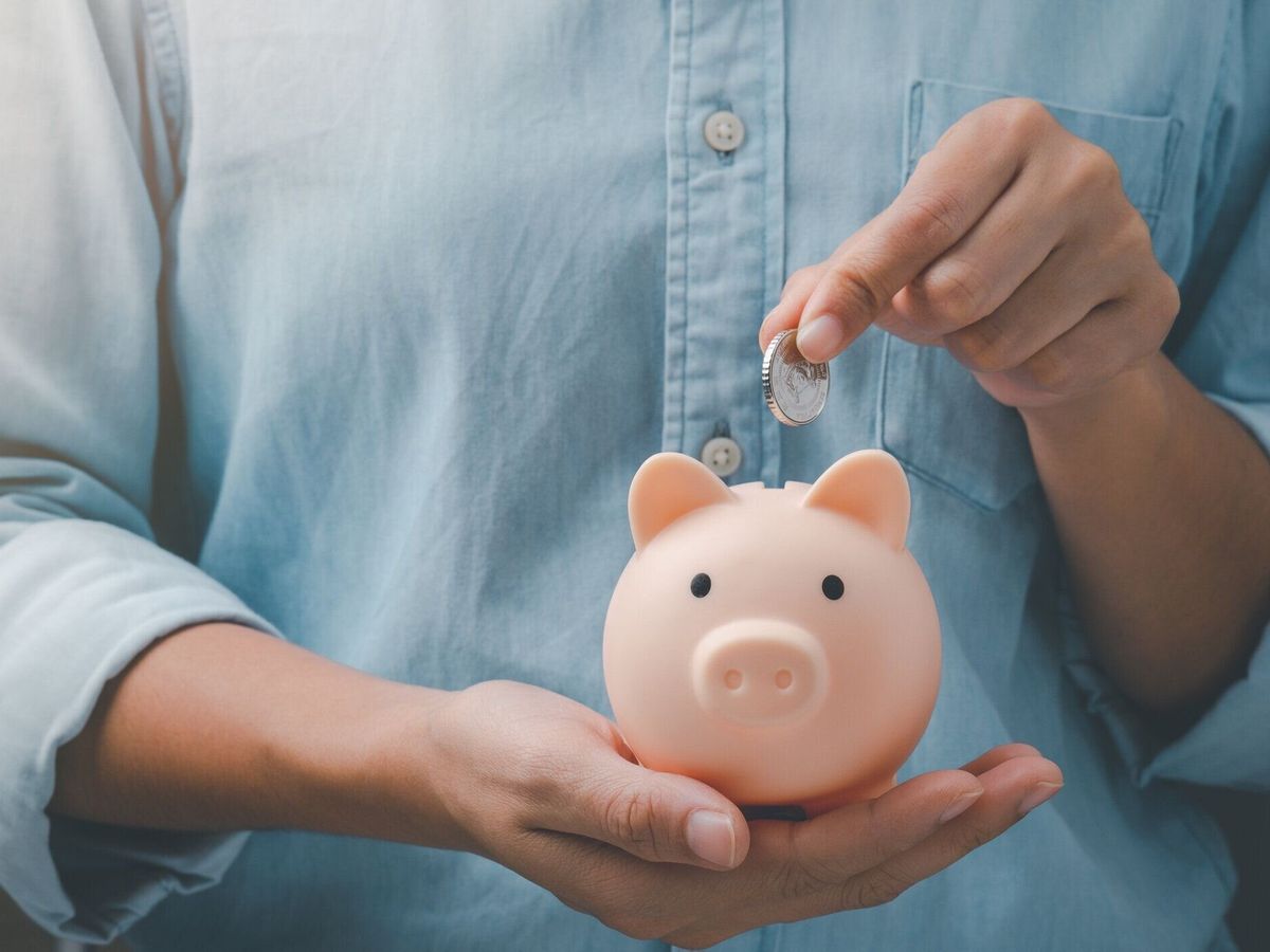 女性の手はピンクの貯金箱にコインを入れます。お金を節約するという概念。