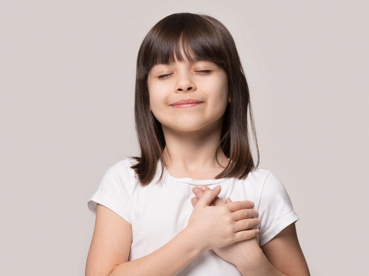 小さな女の子の目を閉じて胸に手をつないで感謝を感じる