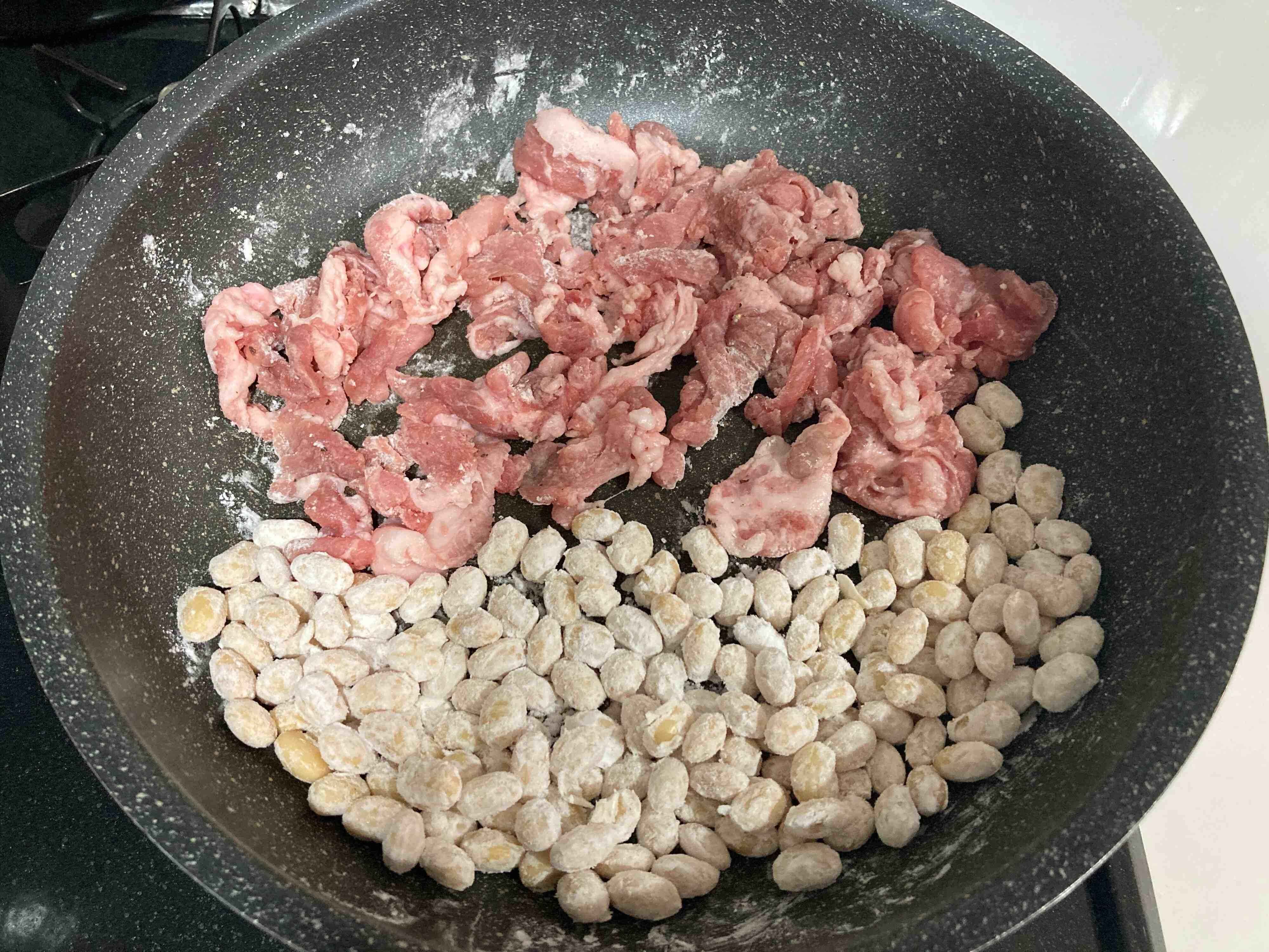 フライパンの上で片栗粉をまぶした豚こまと大豆