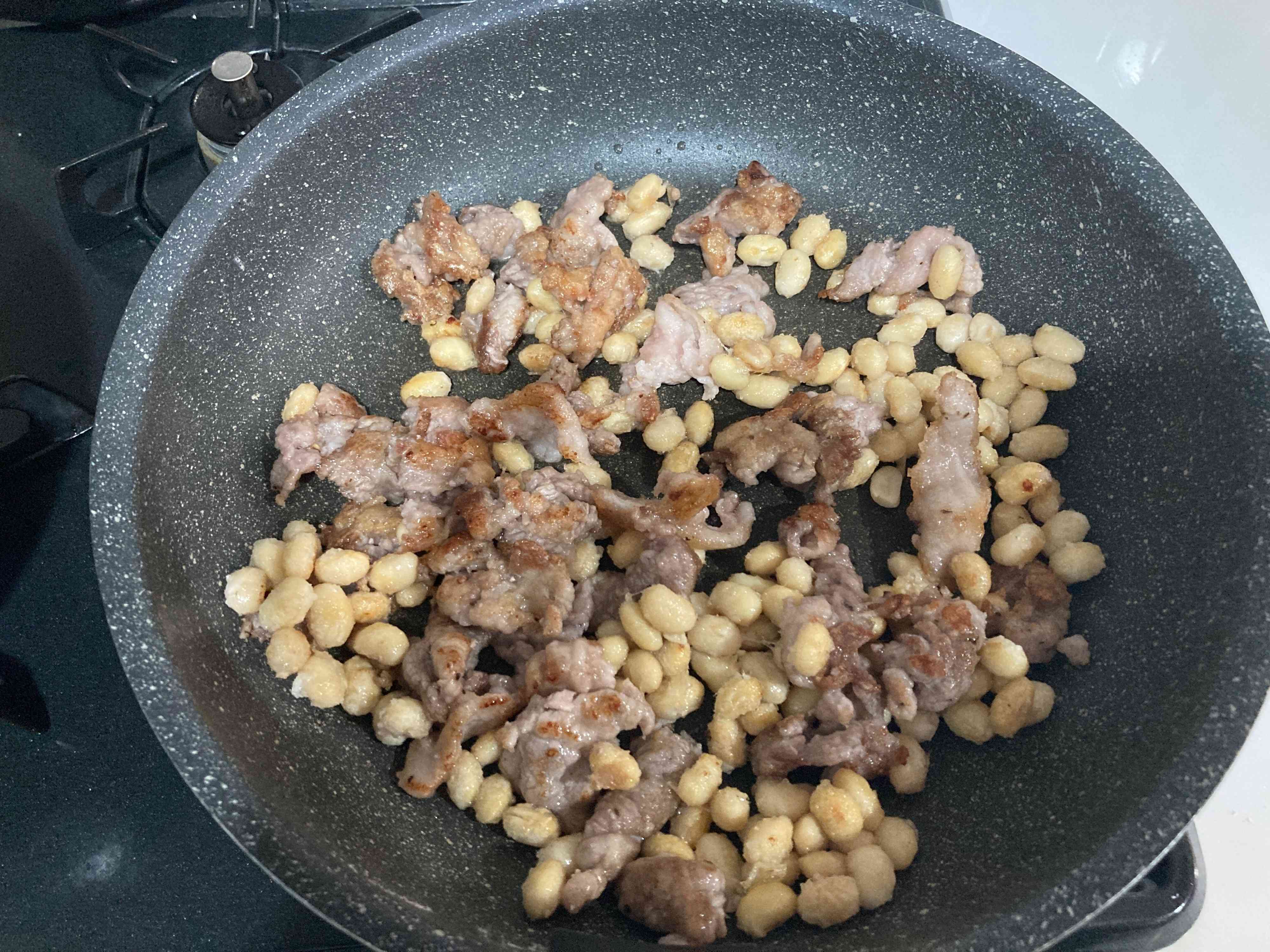 両面焼き色のついた豚こまと大豆を炒めているところ