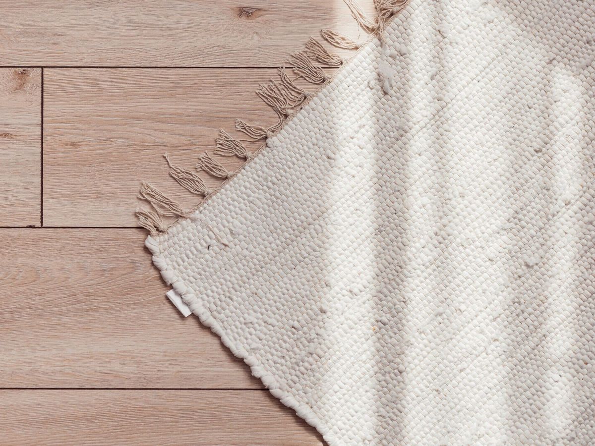 木製の寄木細工の床に籐のベージュのラグ、日当たりの良い、上の景色。