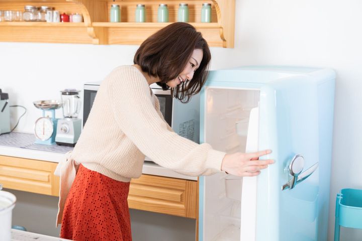 キッチン、冷蔵庫で魅力的なアジアの女性料理
