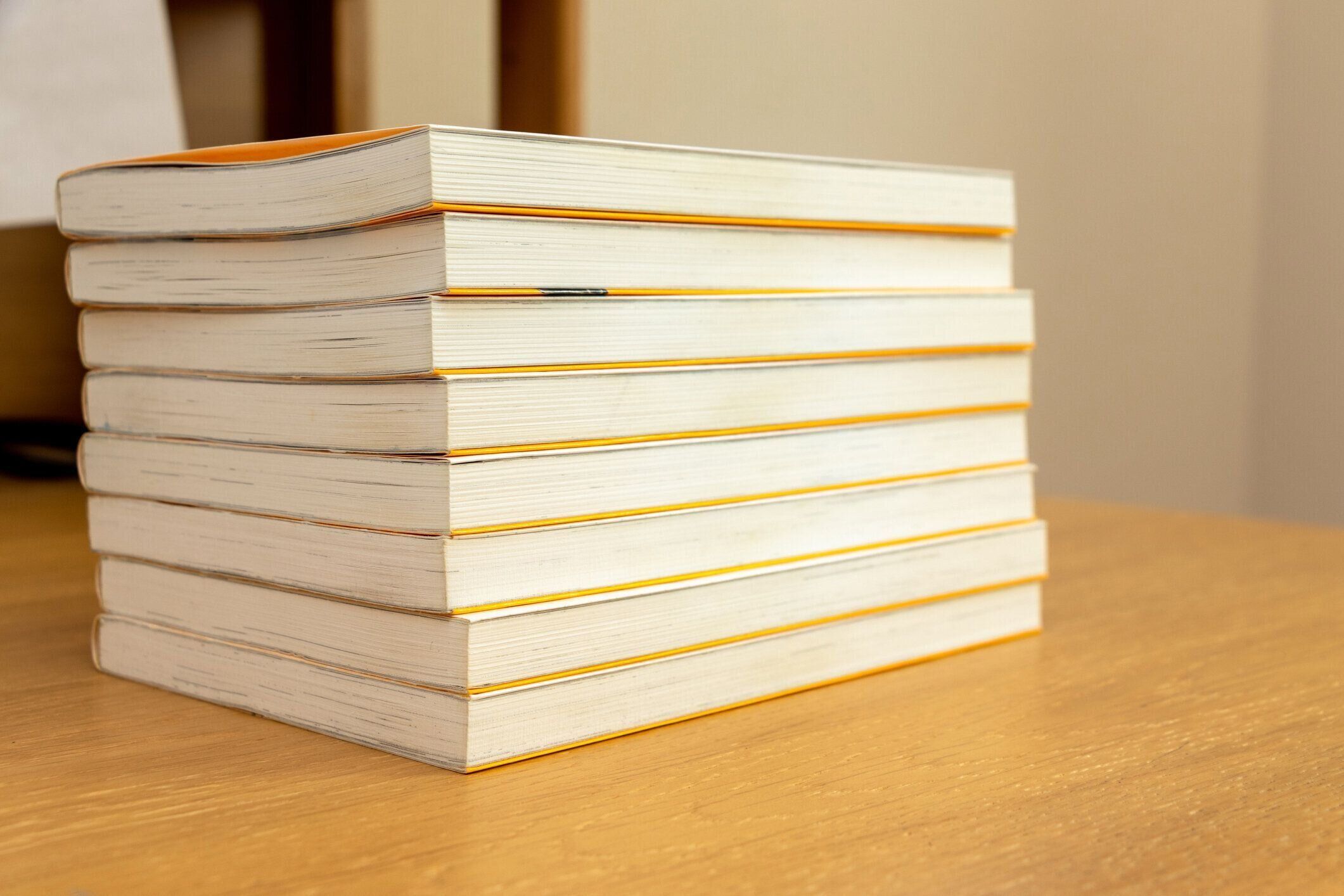 たくさんの本が木製の机の上に積み重ねられています