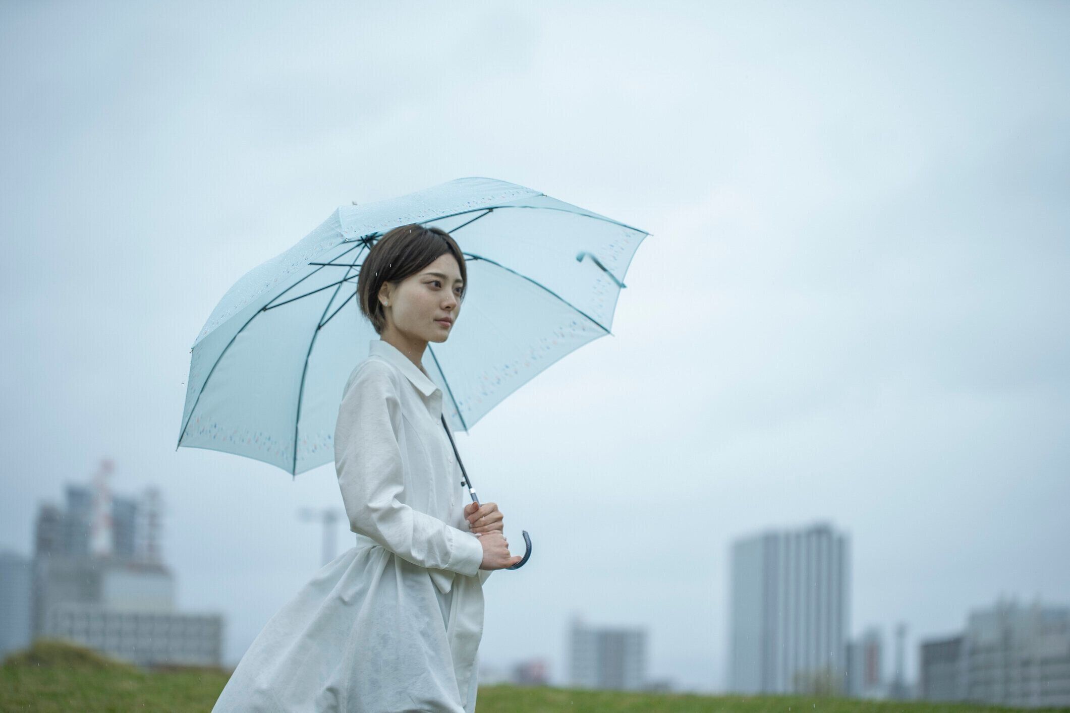 白いドレスを着た若い女性が雨の中で傘を持って歩いている