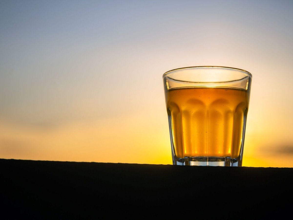 テキストのためのスペースを持つ木製の板の外に泡のないクラフトビールの小さなガラス。日没の背景を持つアルコール飲料のゴールデンサンプル。誰も