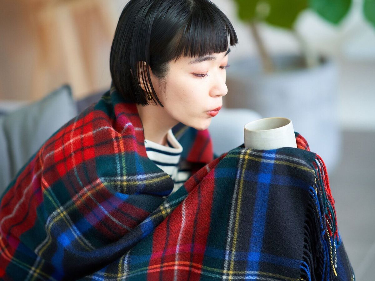 毛布をかぶってマグカップを持つ女性