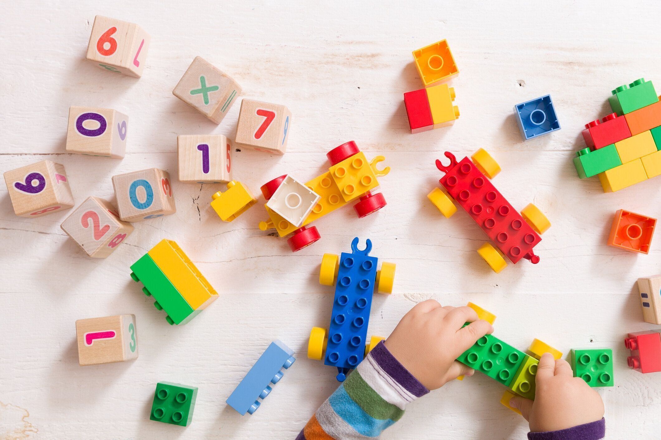 数字と木製白地にカラフルなグッズ レンガと木製キューブと遊ぶ子供。幼児学習番号。おもちゃを取って子供の手。