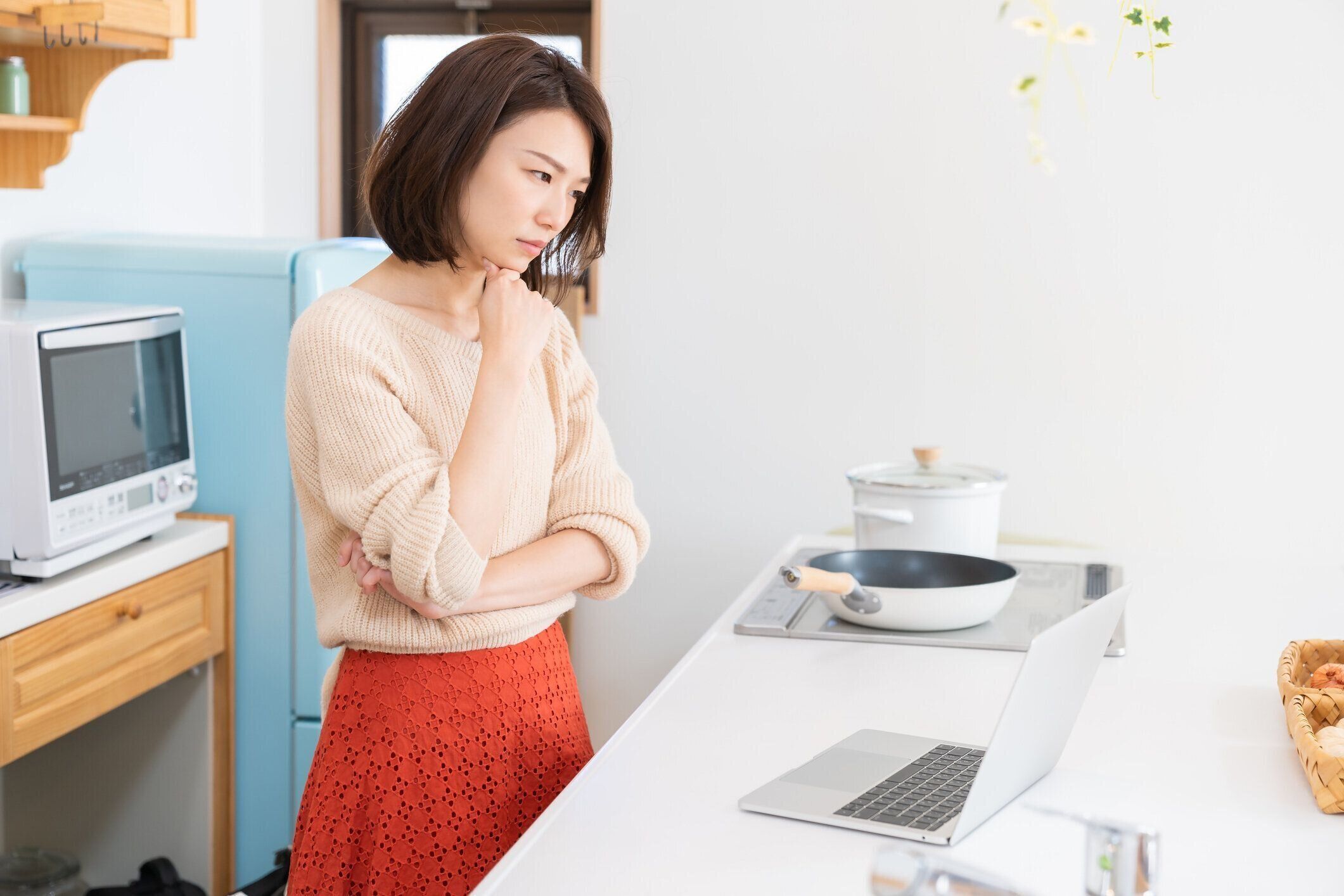 ラップトップ、キッチンを使用して若いアジアの女性は、考え、