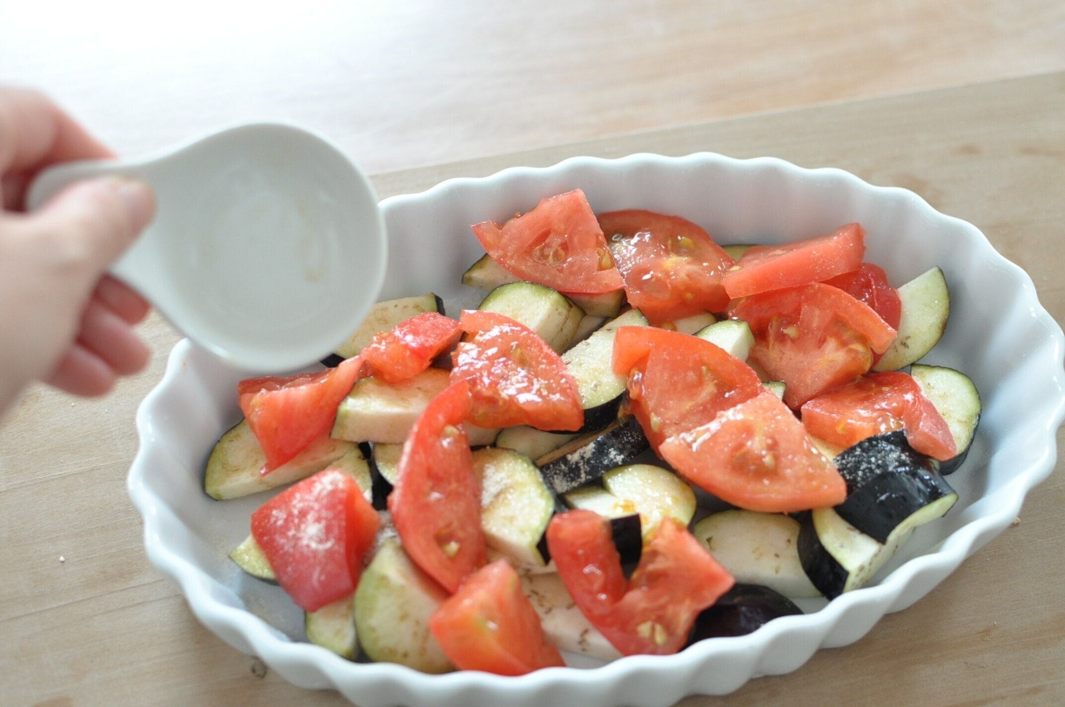 耐熱皿になす、トマトを並べ、コンソメを振りかける様子