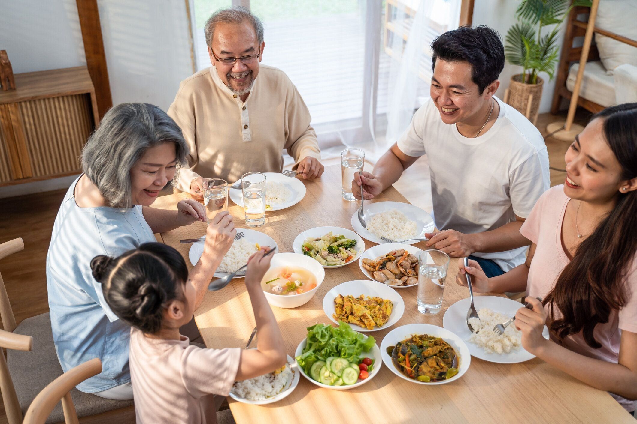大きなアジアの幸せな家族は、一緒に夕食のテーブルで昼食をとって時間を過ごします。小さな子供の娘は、父、母と祖父母と食べ物を楽しむ。多世代関係と家の活動