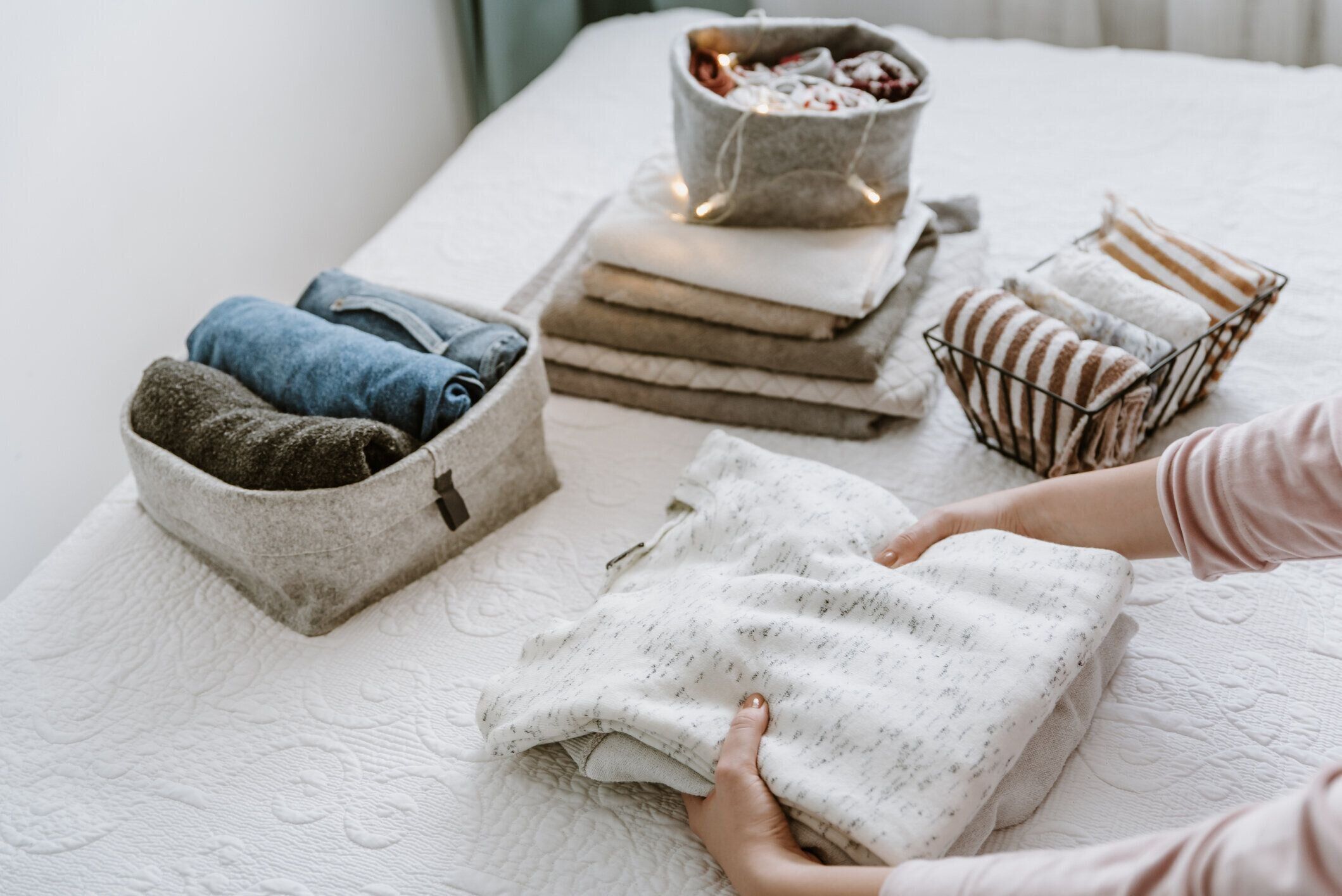 新鮮な洗濯物の積み重ねを折る女性は、箱やバスケットに服やタオルを整理します。