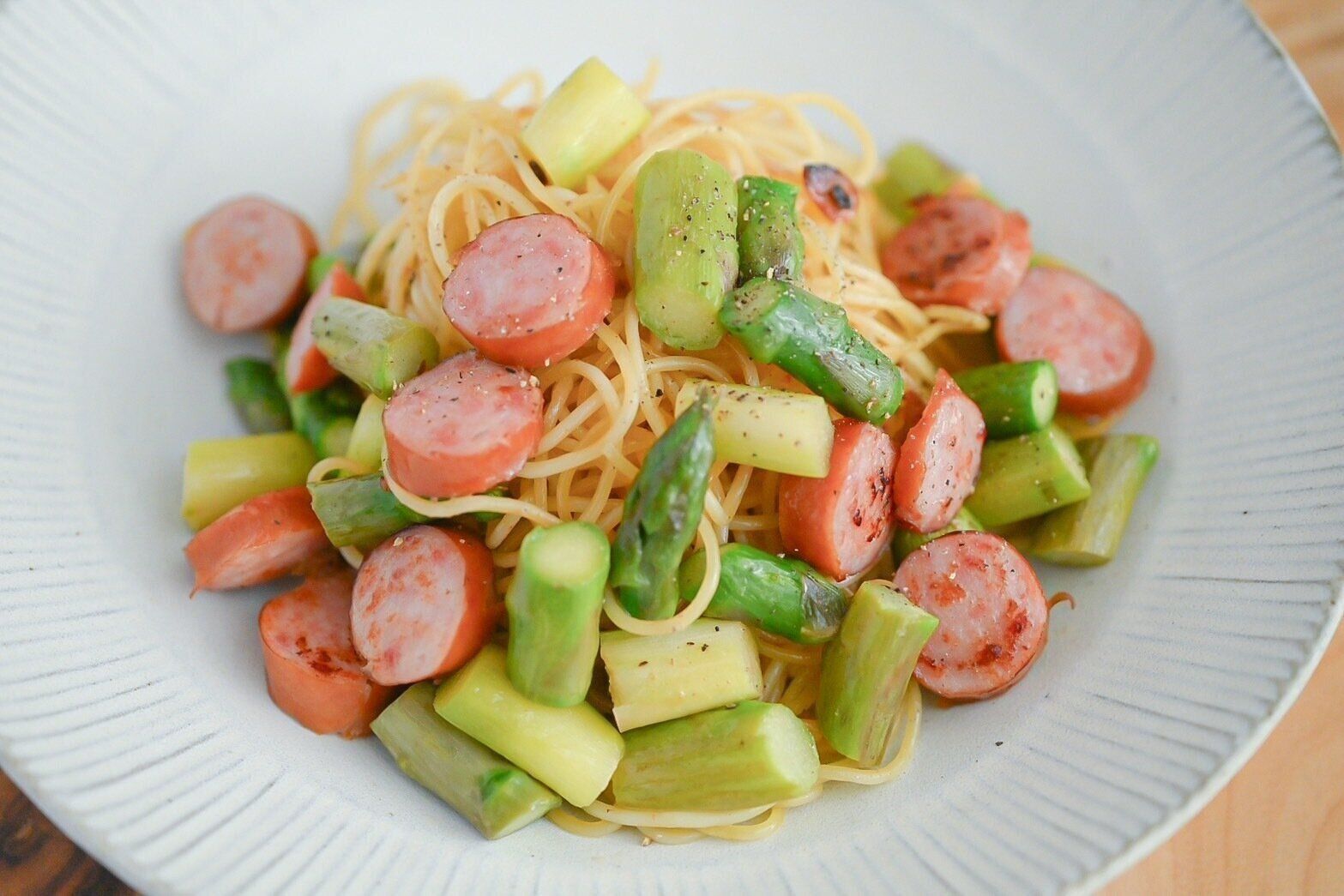 白い皿に盛られたアスパラとソーセージのパスタ