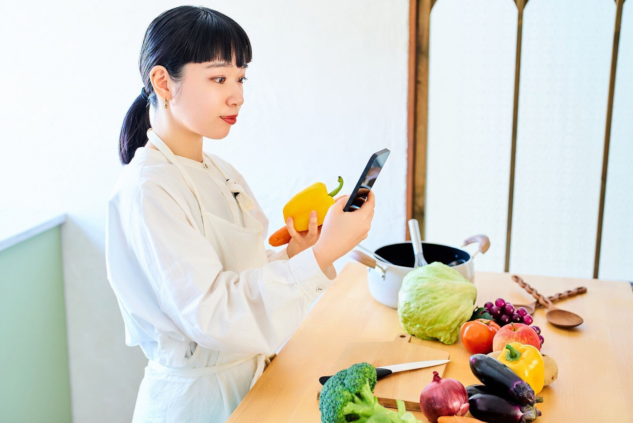 野菜とスマートフォンを手に取る若い女性