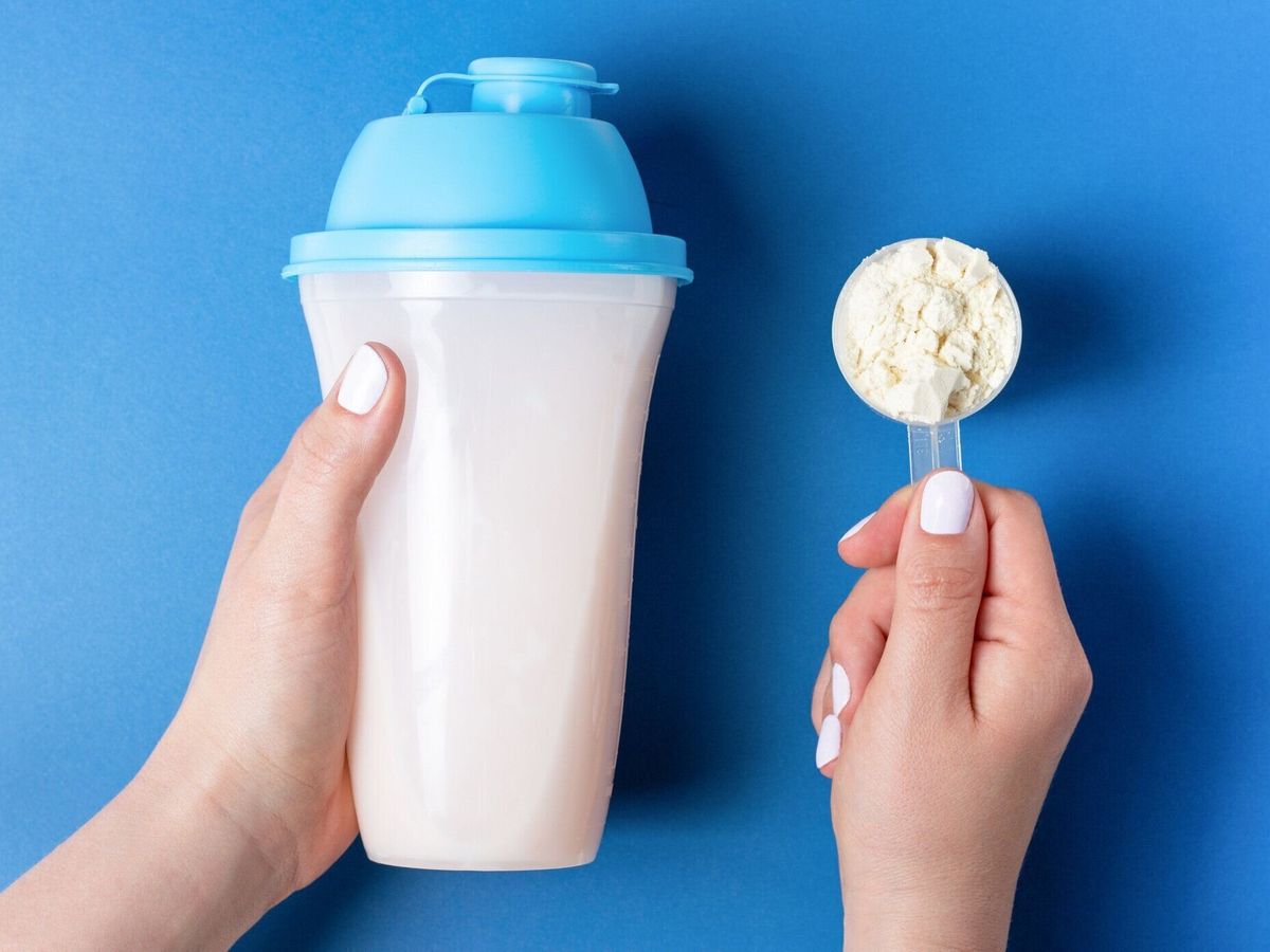 白いマニキュアを持つ女性の手は、タンパク質シェイクのボトルとタンパク質粉末と測定スプーンを保持し、トップビュー