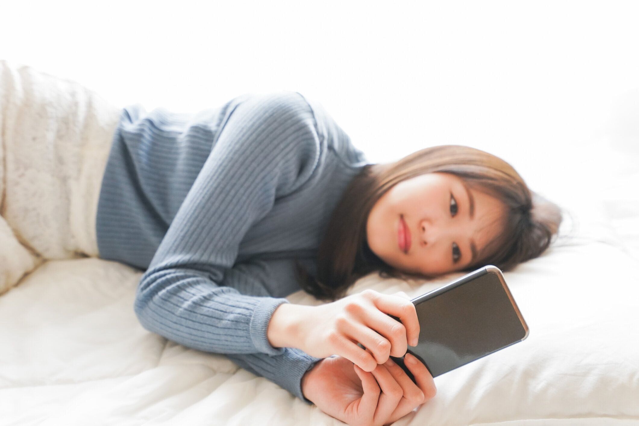 若い女性はベッドで寝る前にスマートフォンを使用します