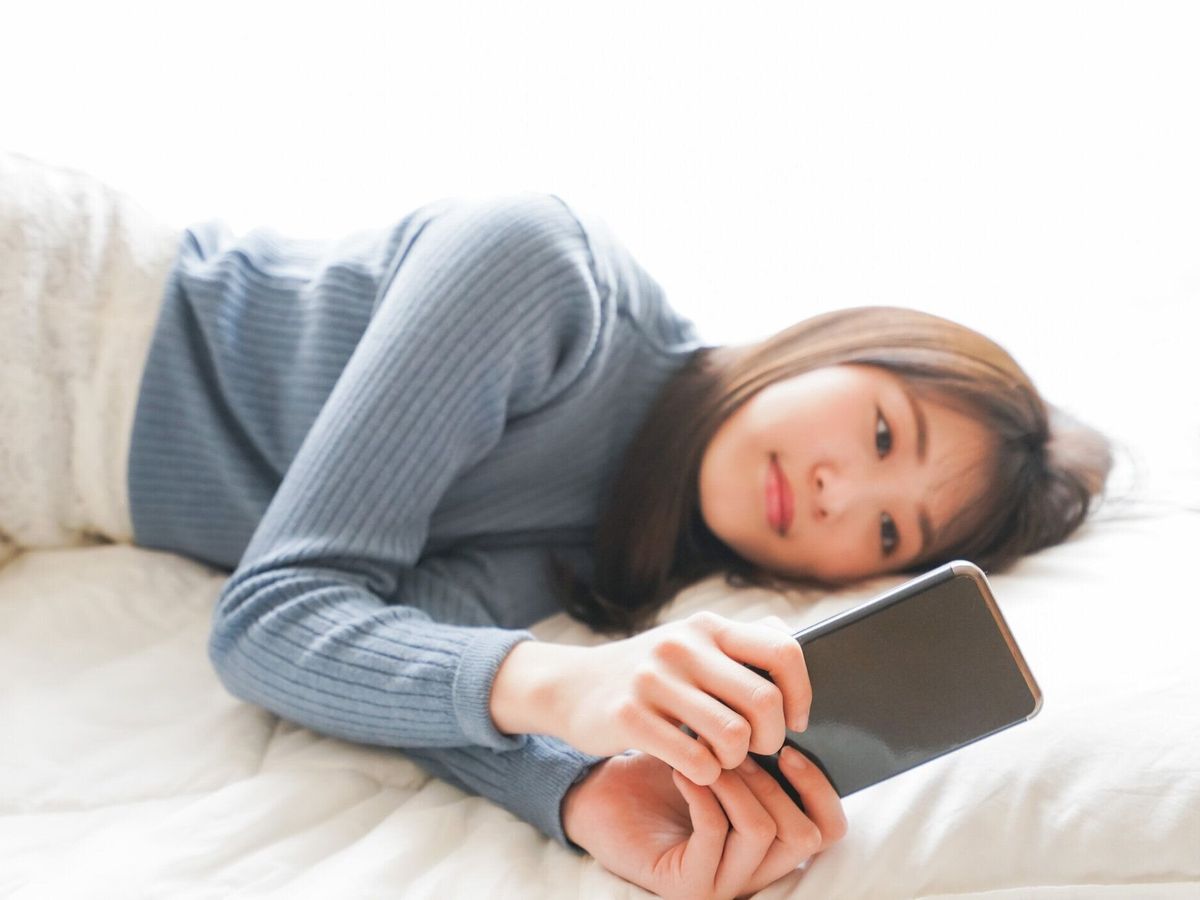 若い女性はベッドで寝る前にスマートフォンを使用します