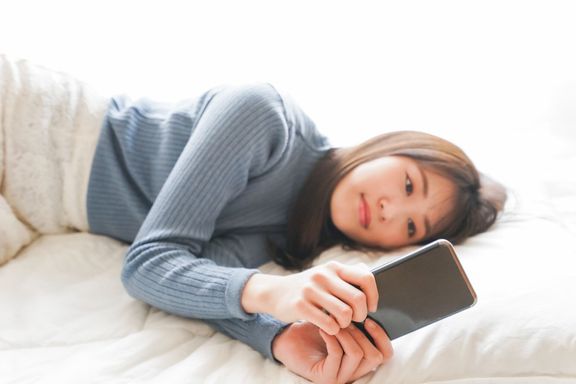 若い女性はベッドで寝る前にスマートフォンを使用します