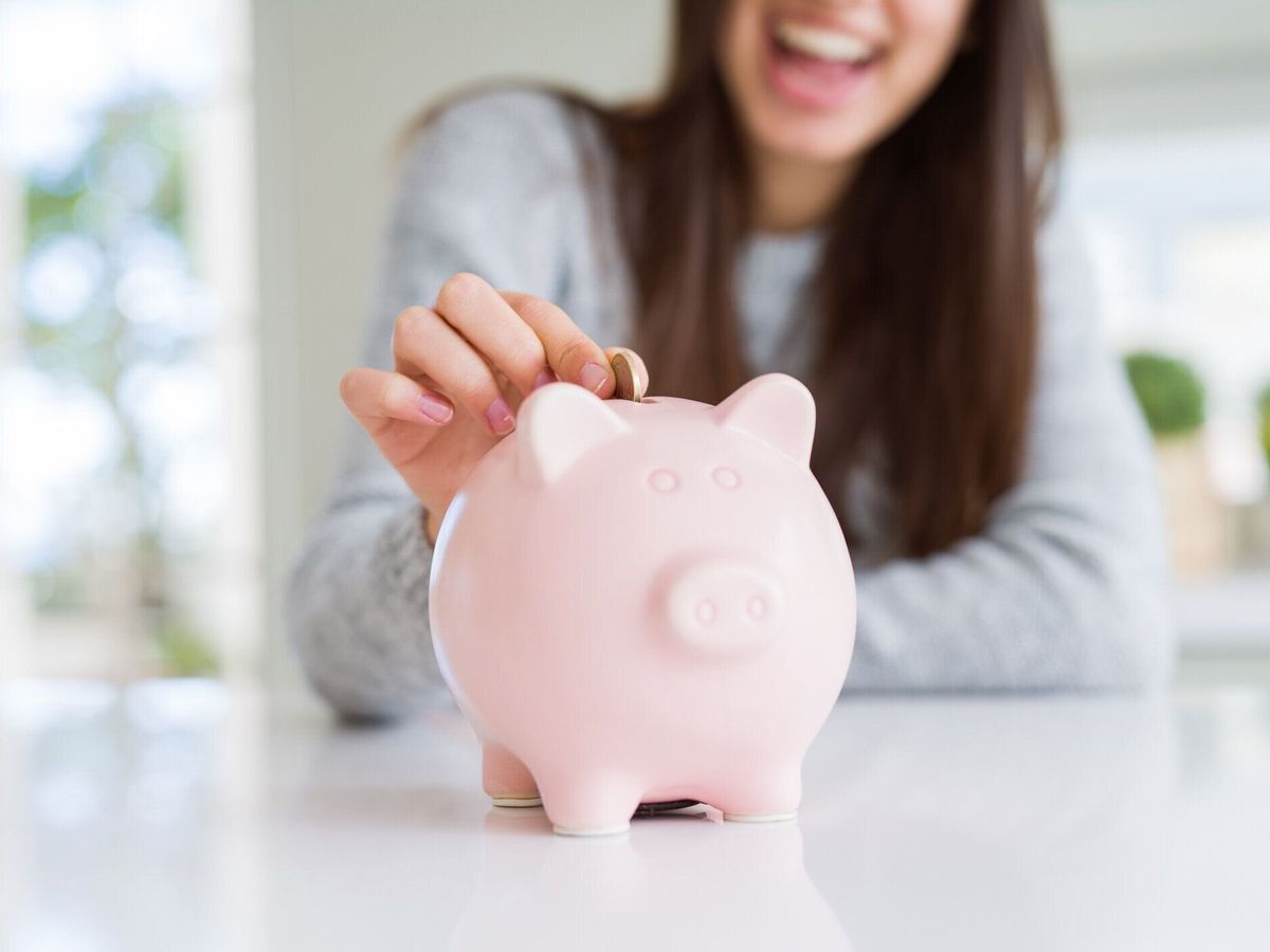 貯金箱の中にコインを入れて笑っている若い女性投資のための貯金