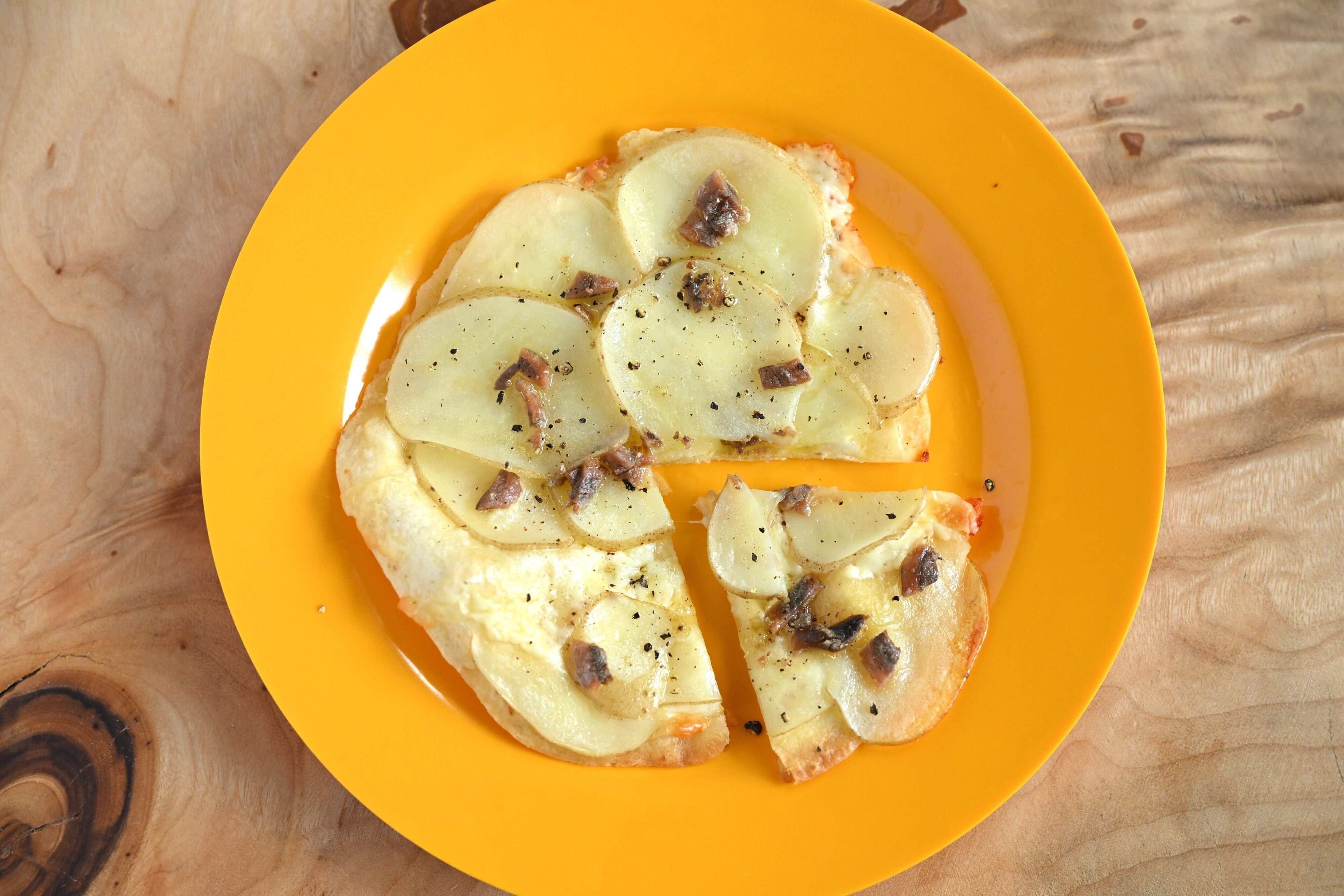 黄色の皿にのったじゃがいもとアンチョビのピザ