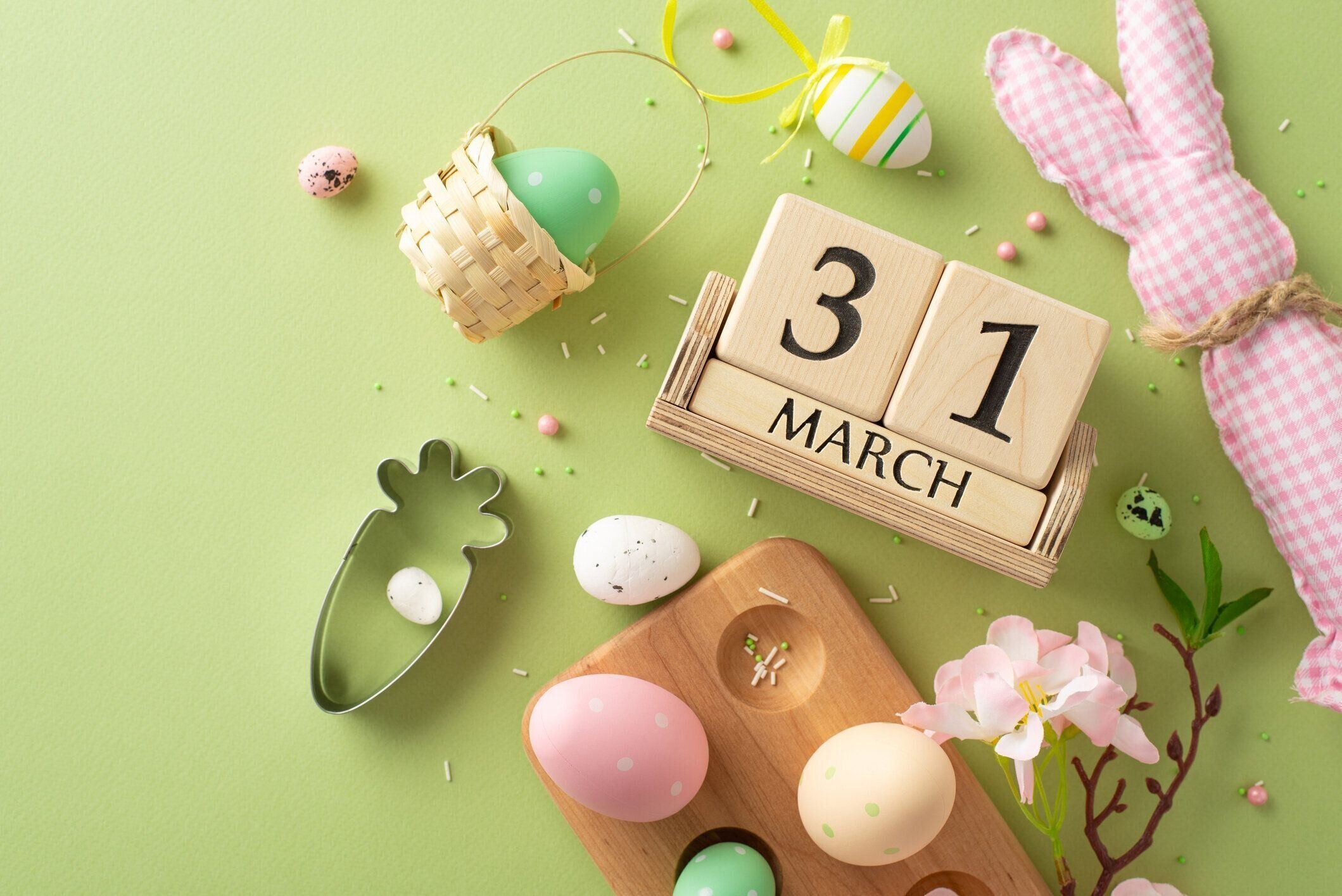 イースター対応の上面図フラットレイ:カラフルな卵、愛らしいウサギの装飾、ベーキングクッキーカッター、木製のナツメヤシの立方体、リンゴの花、パステルグリーンの背景に砂糖を振り