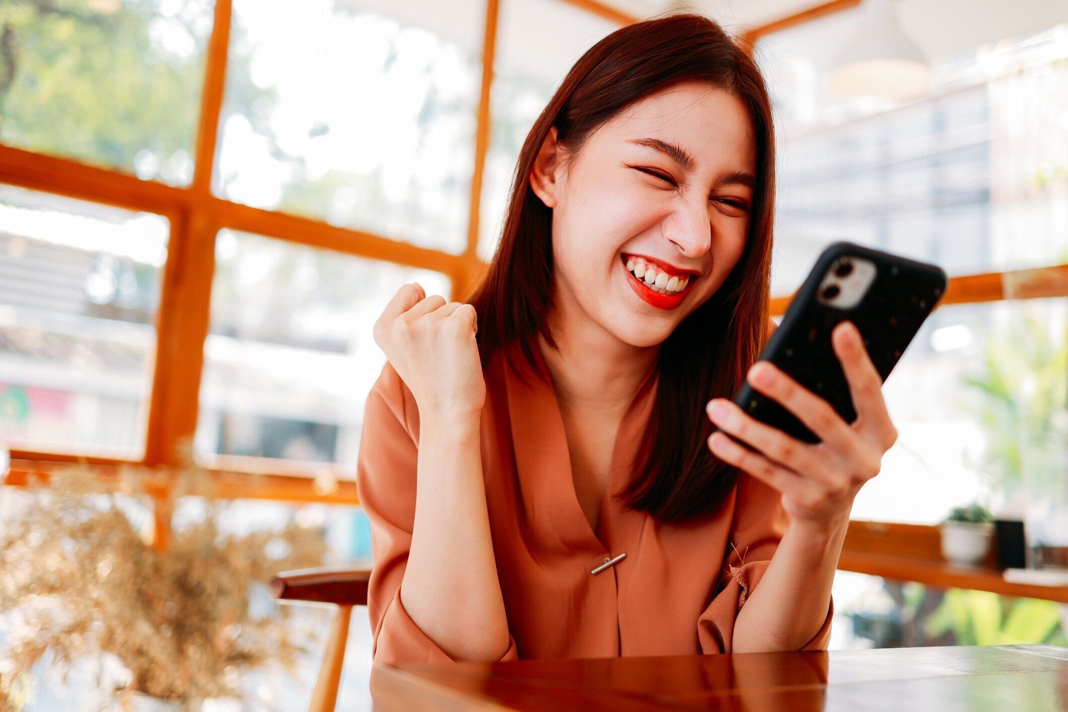 カフェでスマートフォンを使った興奮した女性