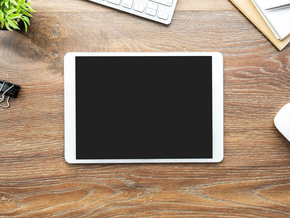 黒いブランクスクリーンが付いている白いタブレットは供給が付いている木製の机のテーブルの上にある。トップビュー、フラットレイ。