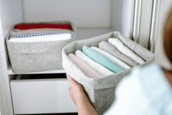 ワードローブで服を整理し、箱にシャツを入れ、バスケットを棚に入れる女性。洗濯後はきちんと折りたたまれた服。ミニマリストライフスタイルのコンセプト