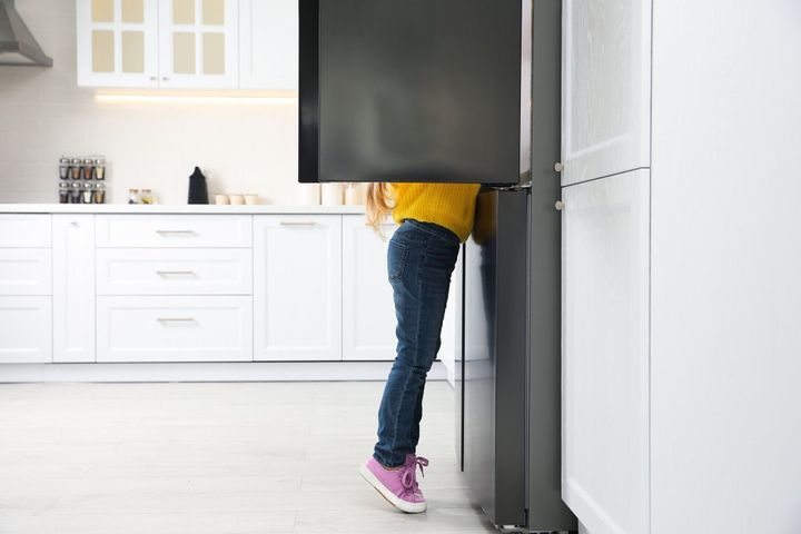 キッチンで開いた冷蔵庫を見ている小さな女の子。テキスト用のスペース