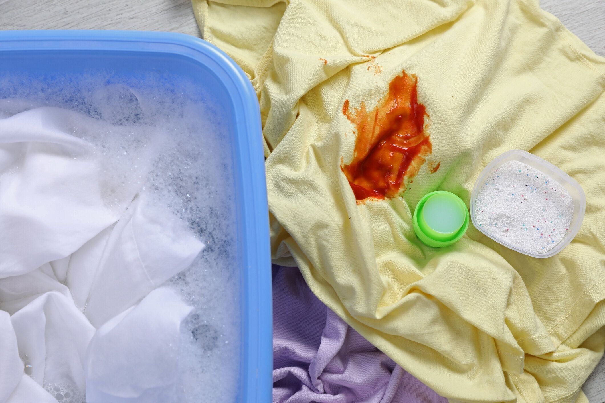 白いシャツを着た洗面器の近くに汚れた衣服と洗剤、上面図。手洗い洗濯物