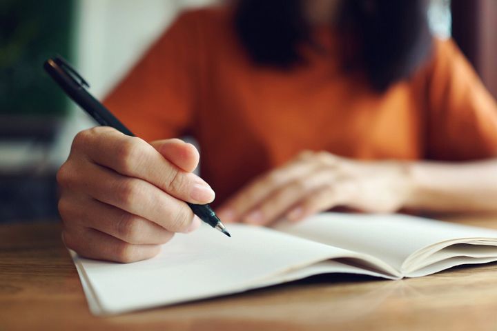ノートに手書きする女性の接写。