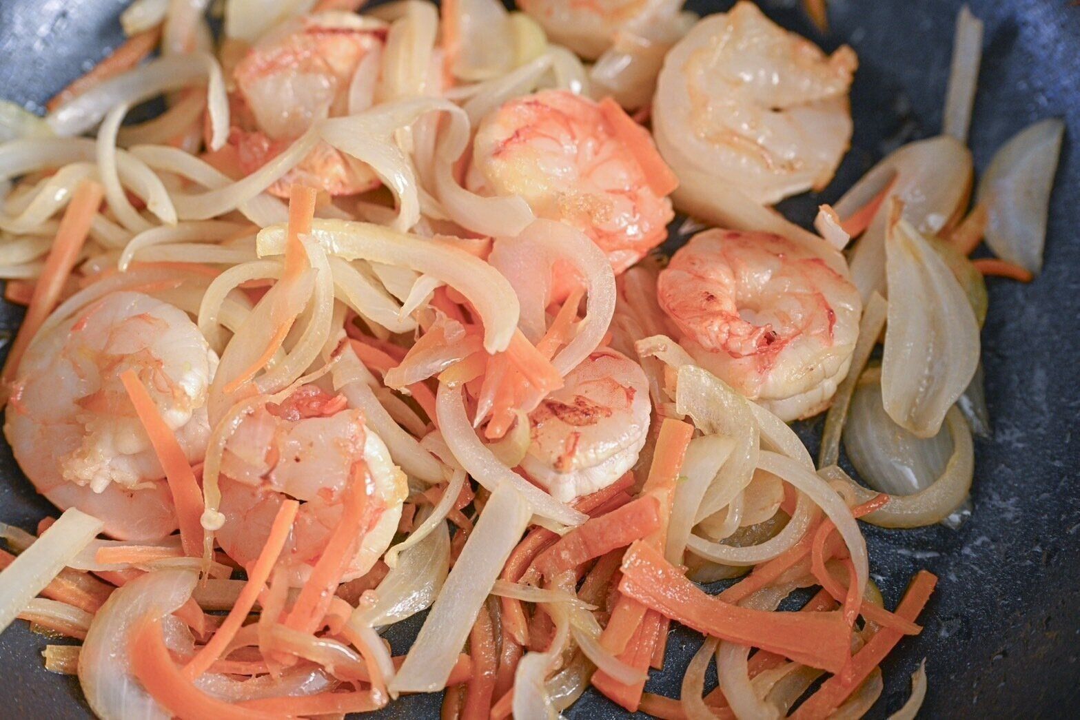 フライパンに入った炒めたえびとにんじんと玉ねぎ